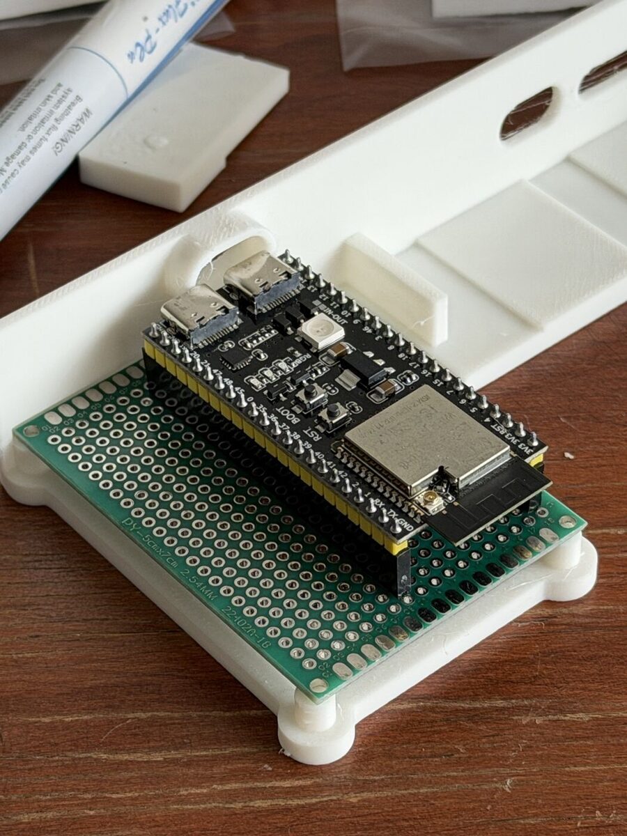A green perfboard with the ESP32 on it, one end held in a groove in a white printed wall