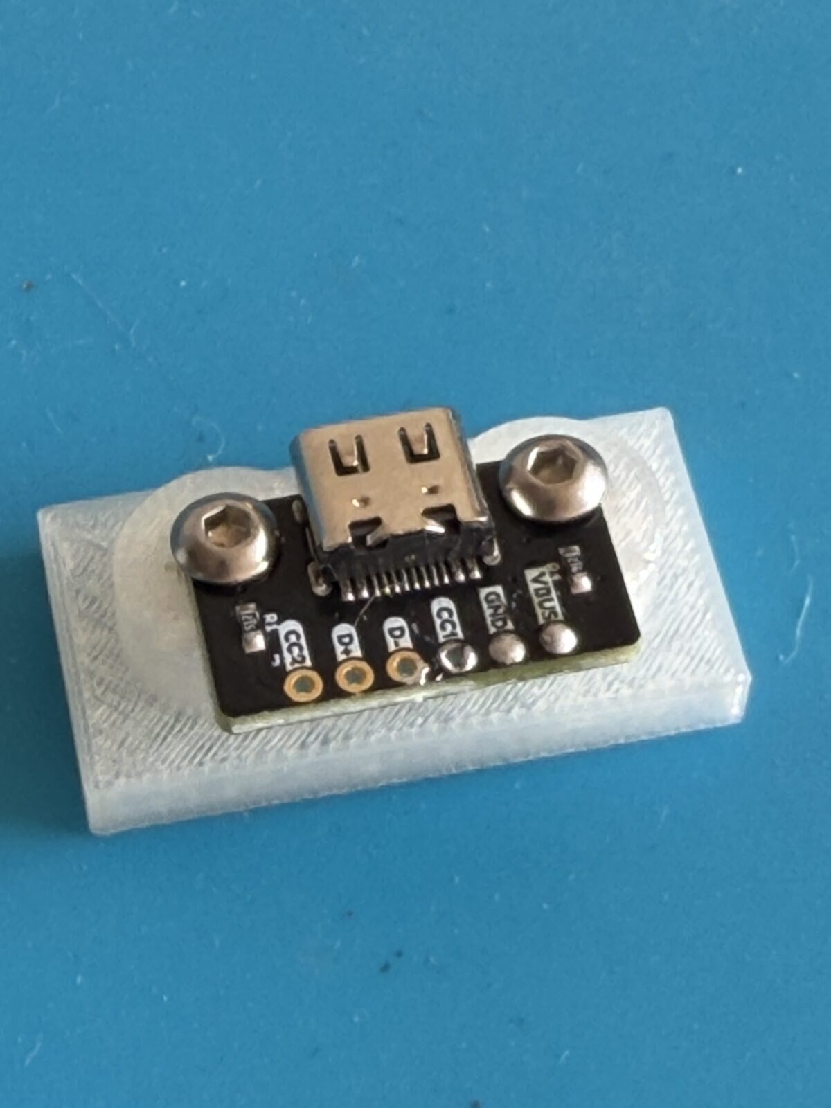 A small clear test print with a USB-C port screwed onto its posts