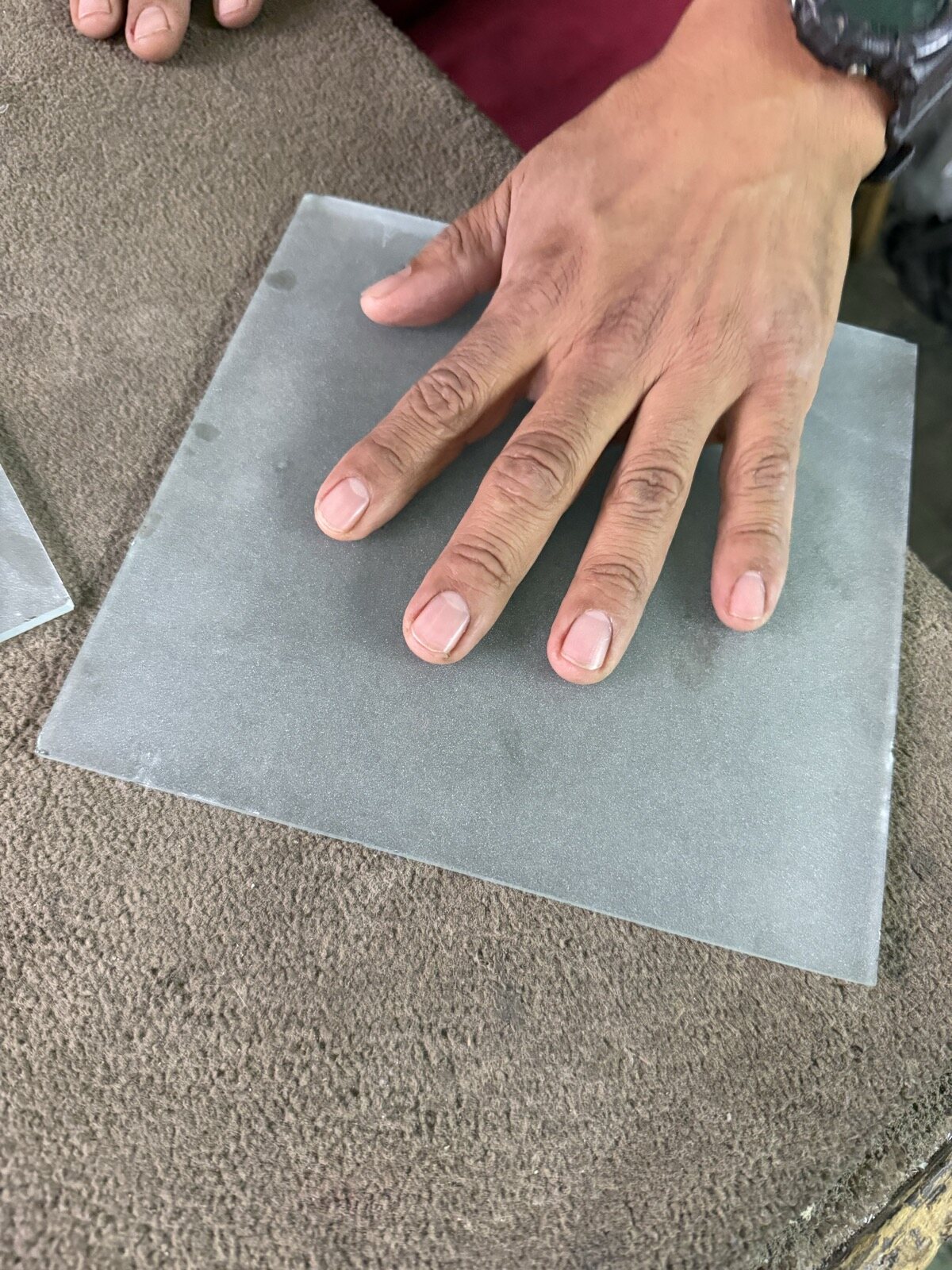 A hand flat on a square of frosted glass at a glass shop