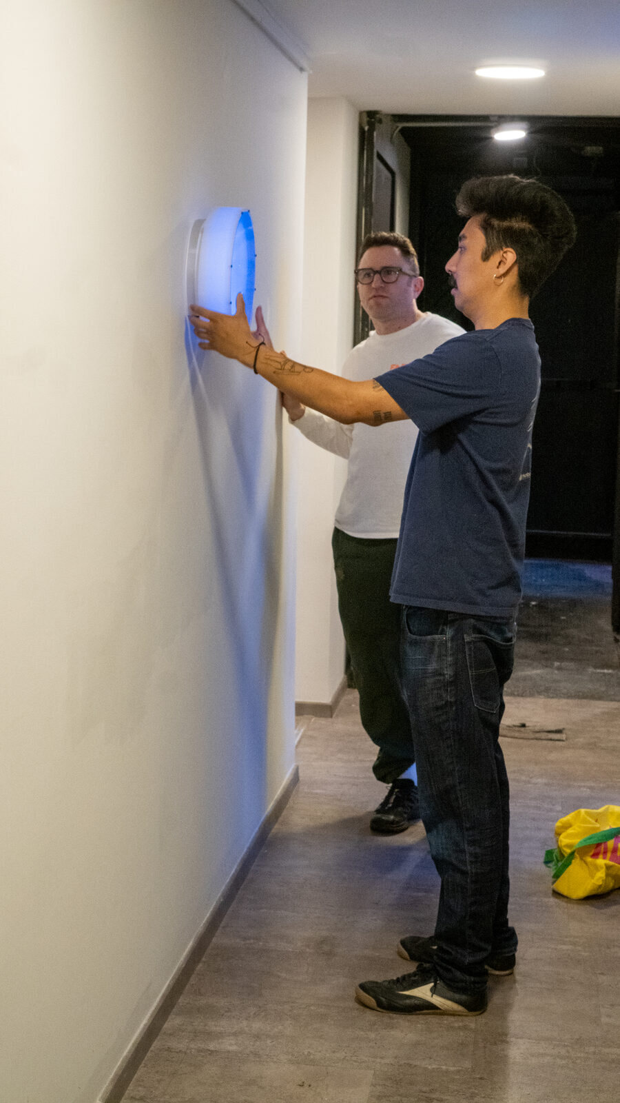 Two men hanging the glowing disk on a wall in the gallery hallway