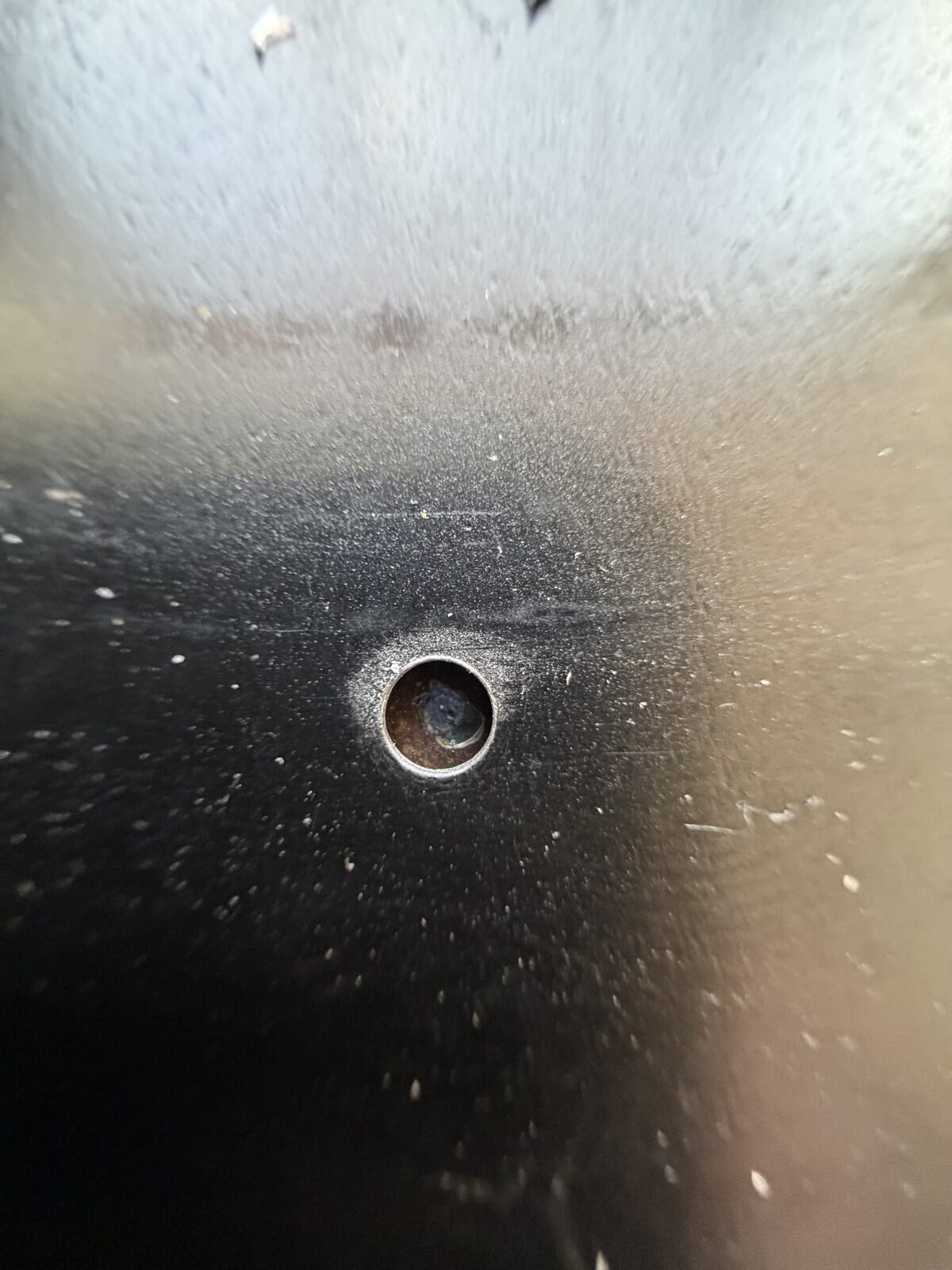A drilled hole through the black steel back of the mirror