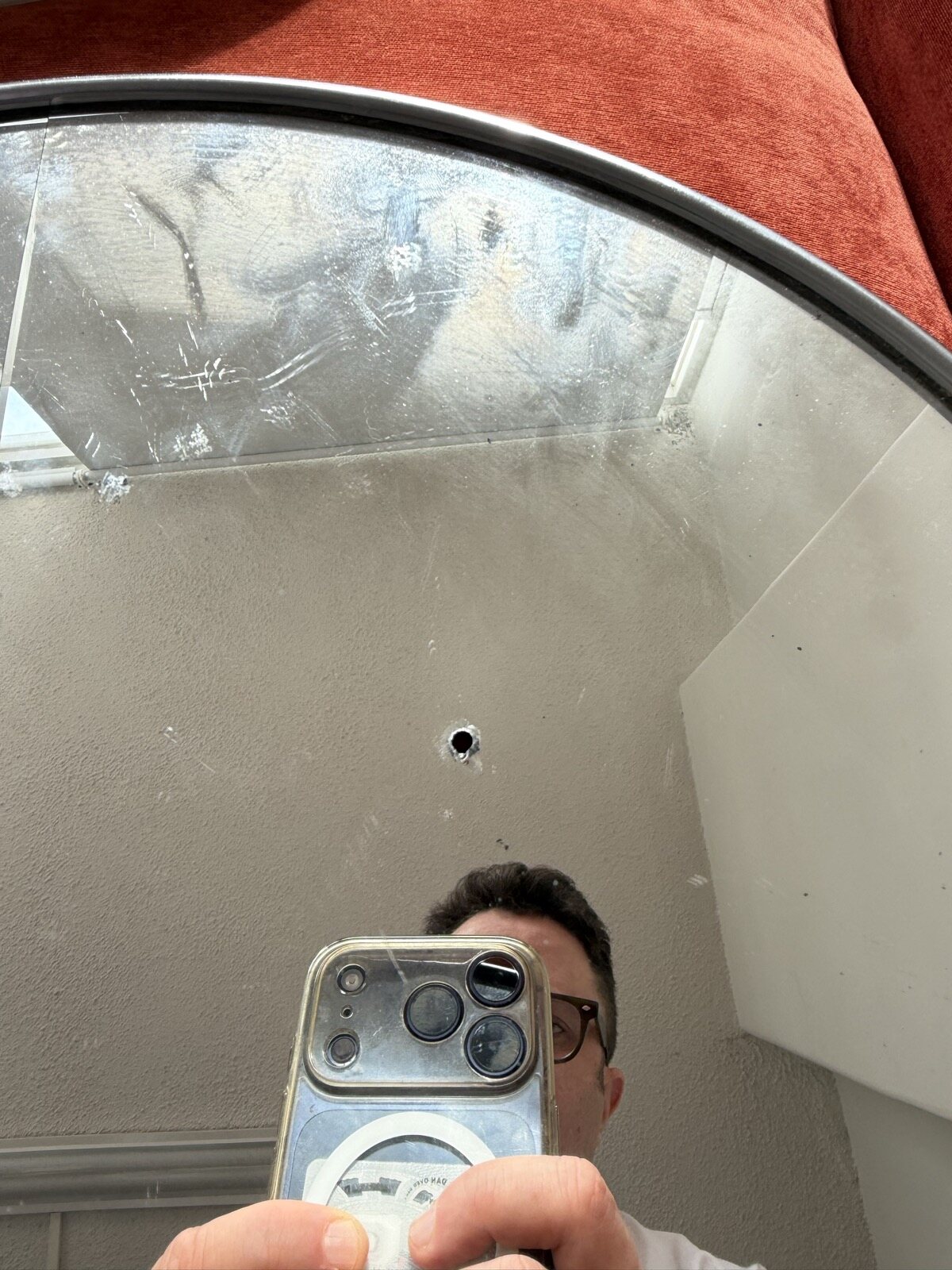 A small clean hole in the cracked mirror, Dan reflected below it taking the photo
