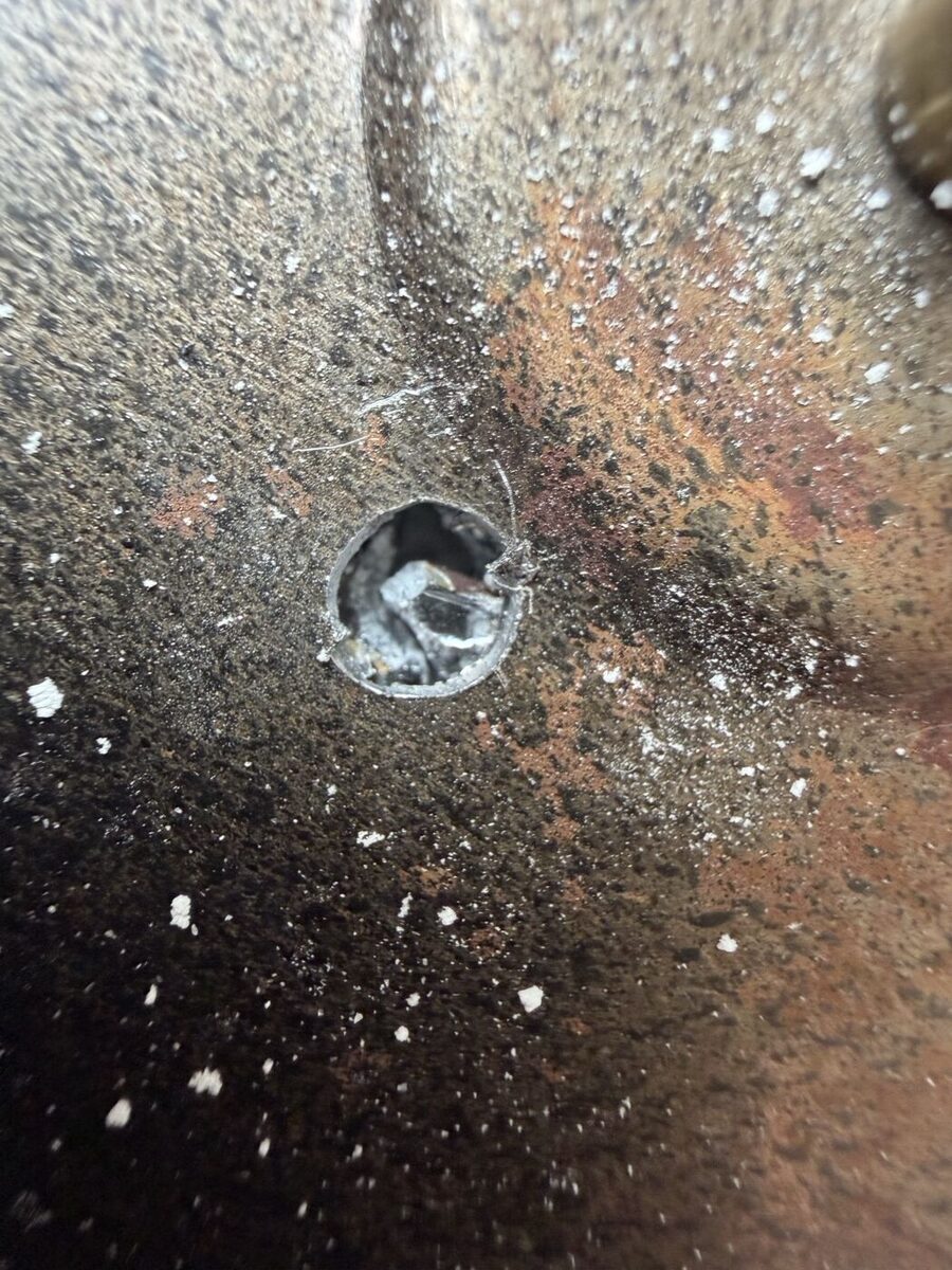 A hole through the back of the mirror's steel pan, glass shards and powder around it