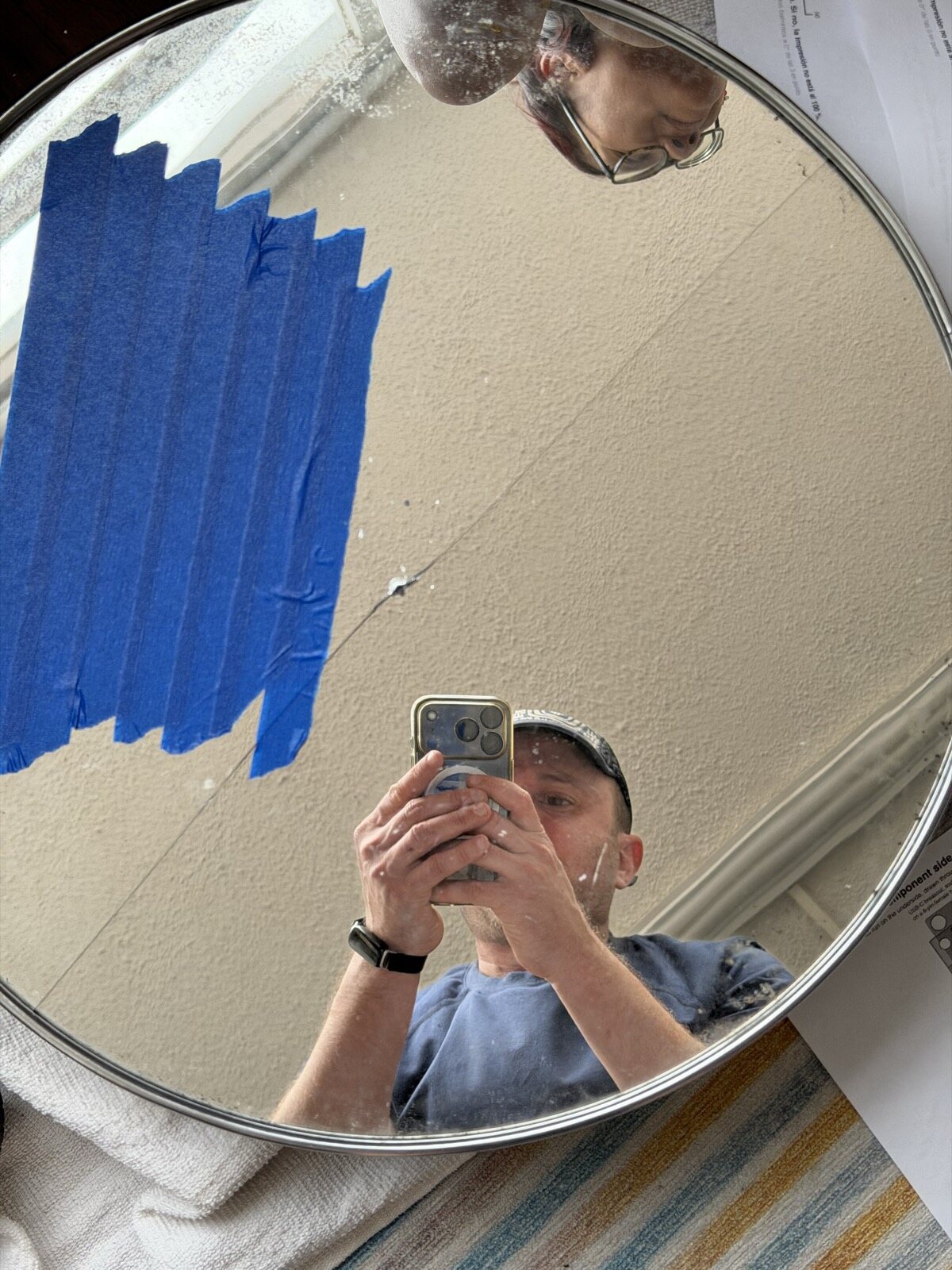 The mirror, cracked from the drilled hole, Dan reflected in it